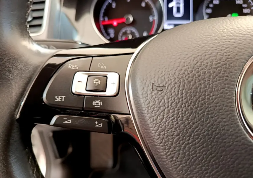 Gros plan sur la partie gauche du volant cuir de la Volkswagen Golf gris clair avec commandes de régulateur adaptatif.