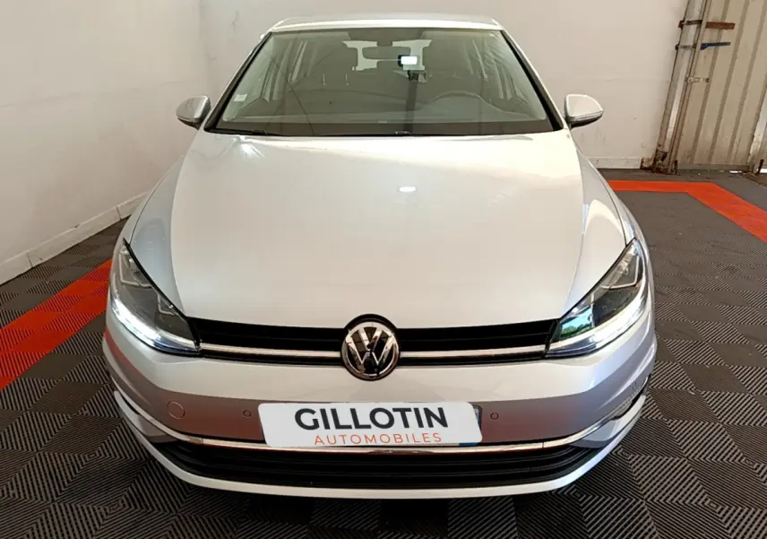 Vue frontale d'une Volkswagen Golf gris clair 2019 avec phares LED allumés dans un garage.
