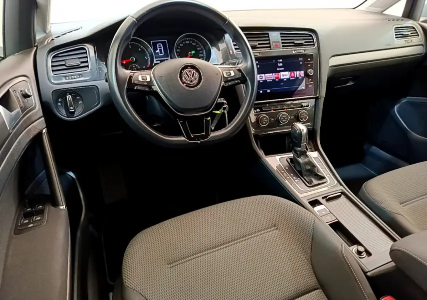 Intérieur de Volkswagen Golf gris clair vu côté conducteur, volant cuir, écran tactile et boîte auto visible.