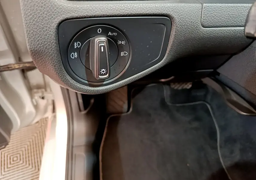 Gros plan sur le bouton de commande des phares noir dans l'habitacle côté gauche d'une Volkswagen Golf gris clair.