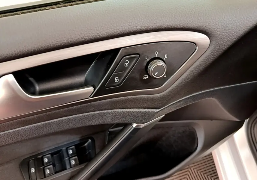 Gros plan sur la porte côté gauche de la Volkswagen Golf gris clair, montrant les commandes des rétroviseurs et des vitres électriques.