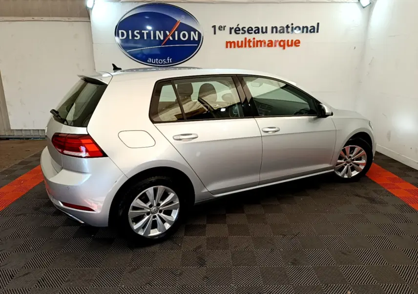 Volkswagen Golf gris clair vue de profil côté gauche dans un showroom avec logo Distinxion en arrière-plan.