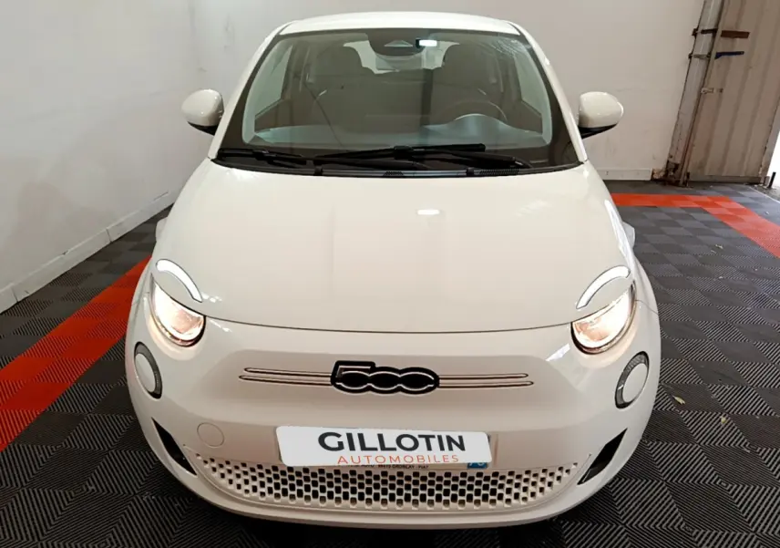 Vue avant d'une Fiat 500 électrique blanche Icône 42kWh avec phares allumés en intérieur.