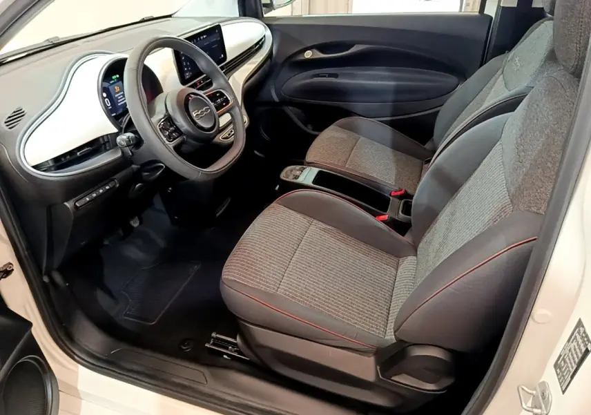 Intérieur avant droit de la Fiat 500 Icône 42kWh 2022 blanc, avec tableau de bord blanc et sièges gris à surpiqûres rouges.