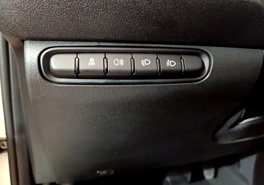 Gros plan sur les boutons de commande des phares et de l'antipatinage dans l'habitacle noir d'une Fiat 500 électrique blanche 2022.