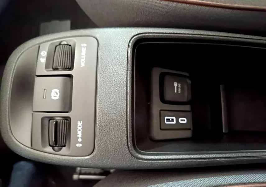 Vue rapprochée de la console centrale noire de la Fiat 500 électrique blanche, avec commandes volume, mode et prises USB et 12V.