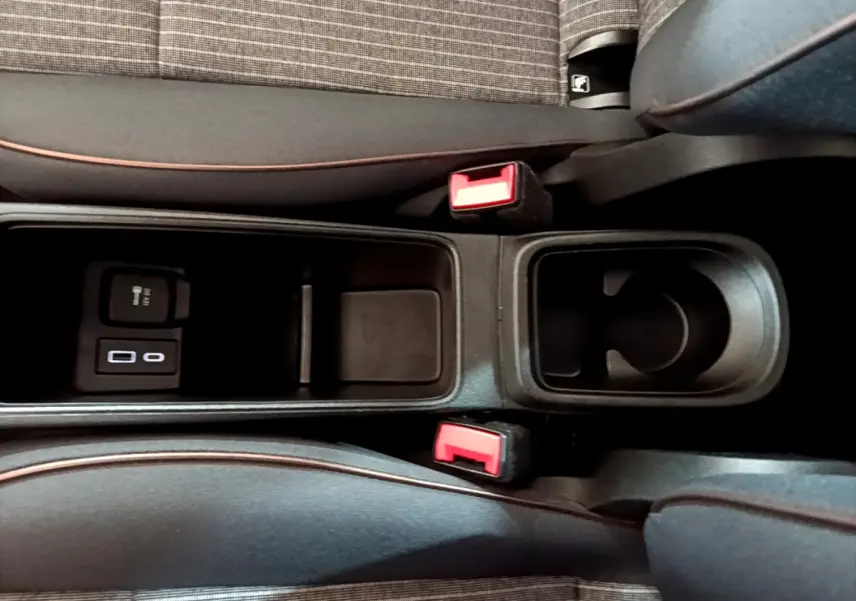 Gros plan sur la console centrale noire de la Fiat 500 électrique blanche, avec porte-gobelet et ports USB visibles.