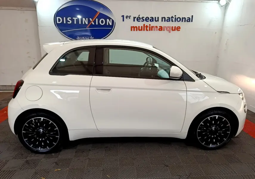 Profil côté droit d'une Fiat 500 électrique blanche 42kWh Icône avec jantes noires stylisées en intérieur showroom.