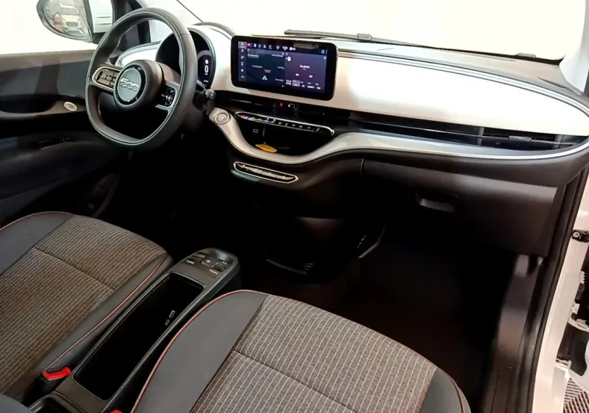 Vue intérieure côté conducteur de la FIAT 500 électrique blanche, tableau de bord moderne avec écran tactile central.