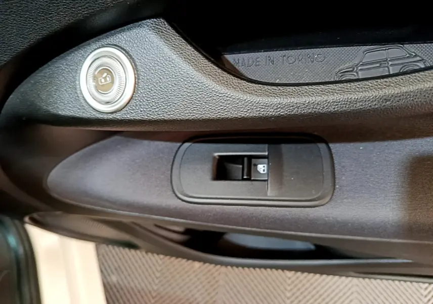 Gros plan sur la commande de lève-vitre côté gauche de la porte noire intérieure d'une Fiat 500 électrique blanche.