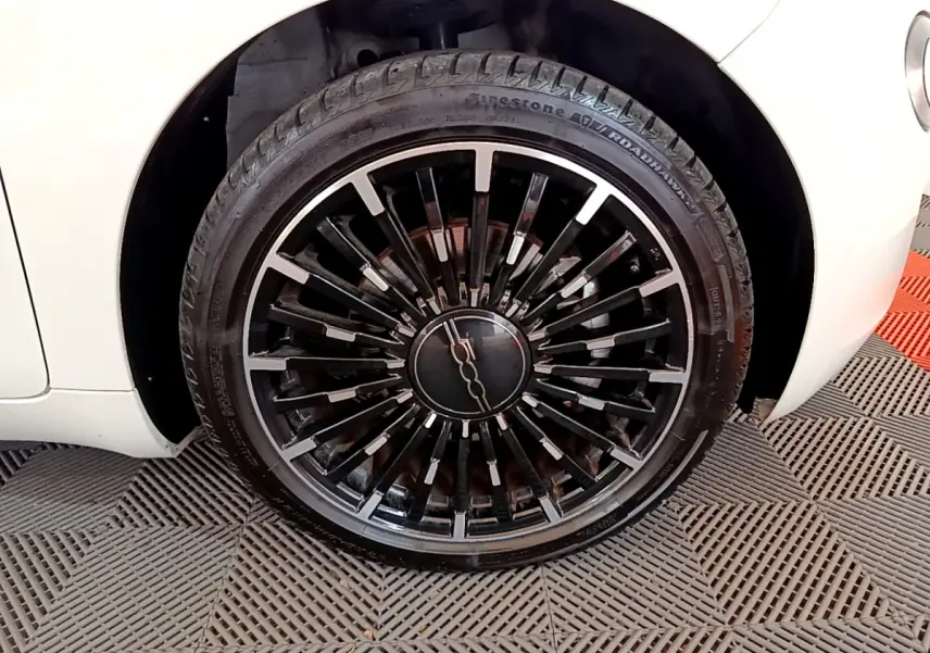 Gros plan sur la roue avant droite noire à jantes stylisées d'une FIAT 500 électrique blanche 2022.