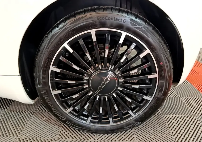 Gros plan sur la roue avant gauche de la FIAT 500 blanche électrique, jante noire à rayons fins avec logo central.