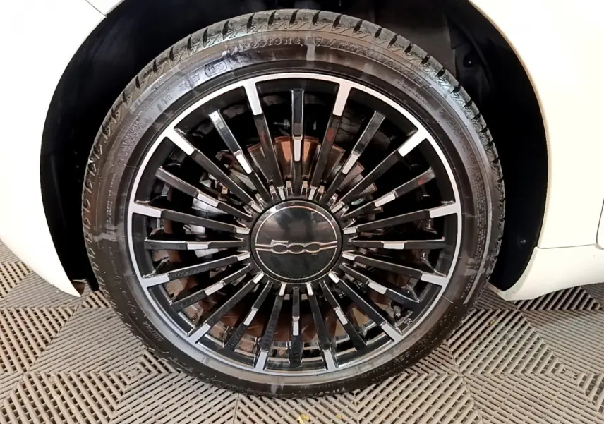 Gros plan sur la roue avant droite blanche d'une FIAT 500 électrique avec jante noire à rayons fins et logo central 500.