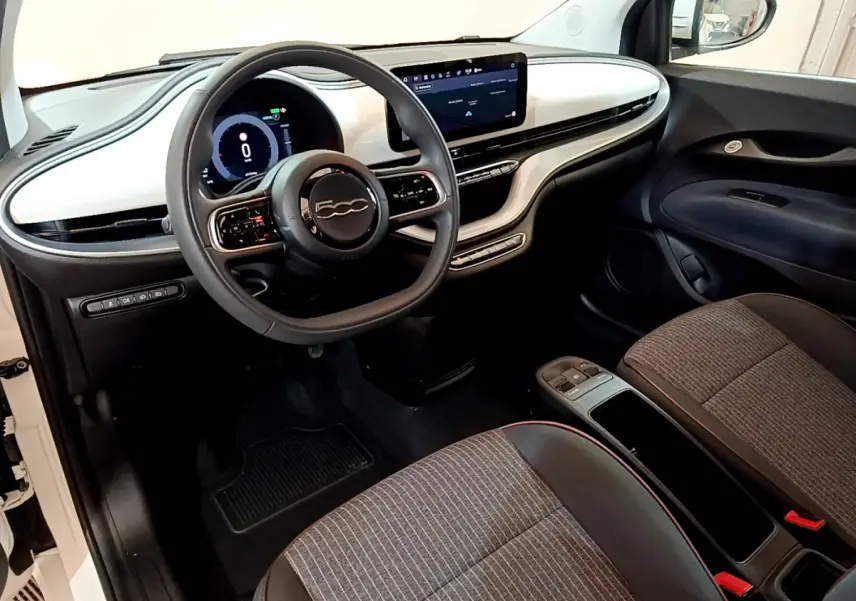 Vue intérieure côté conducteur de la Fiat 500 électrique blanche, tableau de bord moderne avec écran tactile central.