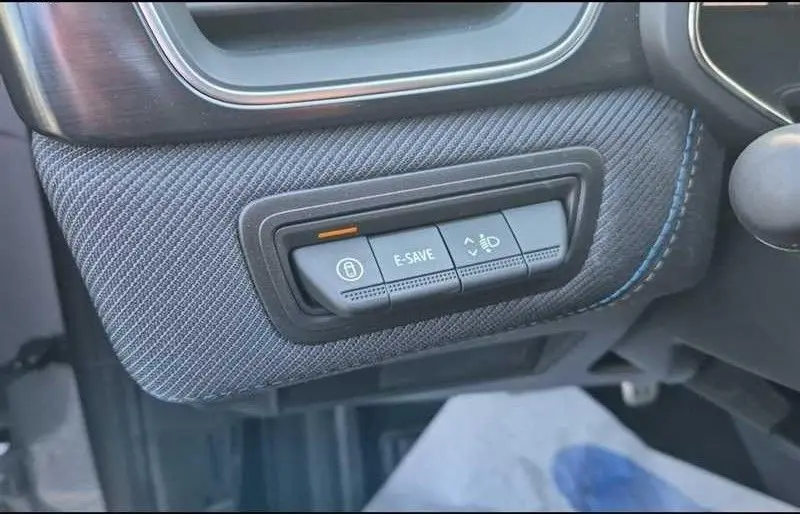 Gros plan sur les commandes E-SAVE et frein de stationnement intégrées dans le tableau de bord gris texturé du Renault Captur hybride.
