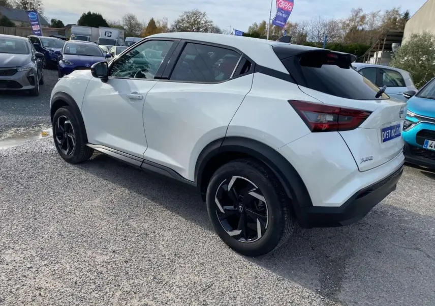 Nissan Juke blanc perle vu en 3/4 arrière droit, avec jantes noires et toit noir contrastant, stationné en extérieur.