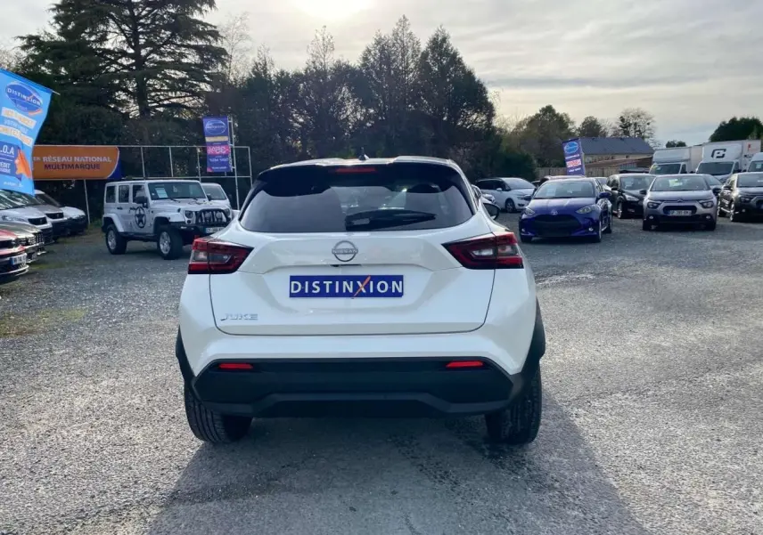 Vue arrière d'un Nissan Juke blanc perle 2024 garé sur un parking avec logo Distinxion visible sur le coffre.