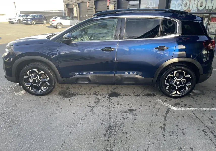 Profil latéral droit du Citroën C5 Aircross hybride bleu Eclipse, avec jantes alliage 18 pouces biton et barres de toit noires.