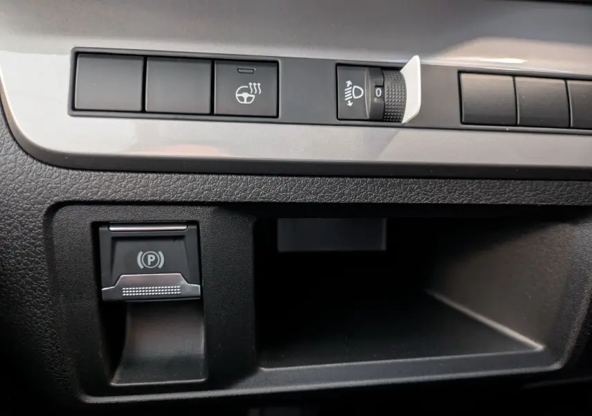Gros plan sur les commandes noires du tableau de bord du Peugeot Traveller 2.2 180 EAT8 XL Business, avec bouton de frein à main électrique.