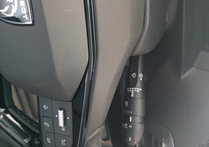 Détail du volant noir de Peugeot Traveller 2026 avec commandes intégrées et logo lion visible.