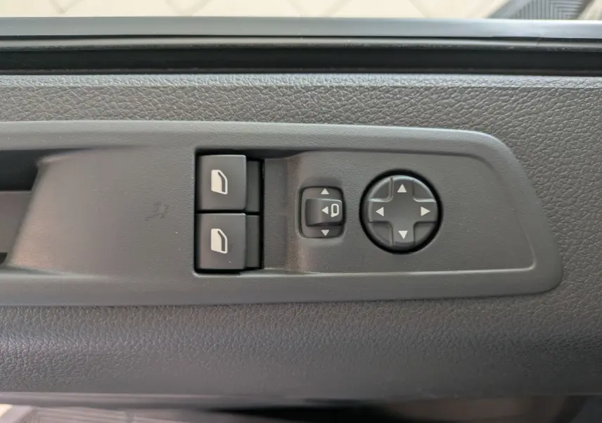 Boutons de réglage des rétroviseurs et des vitres sur la porte intérieure d’un Peugeot Traveller noir, vue rapprochée.