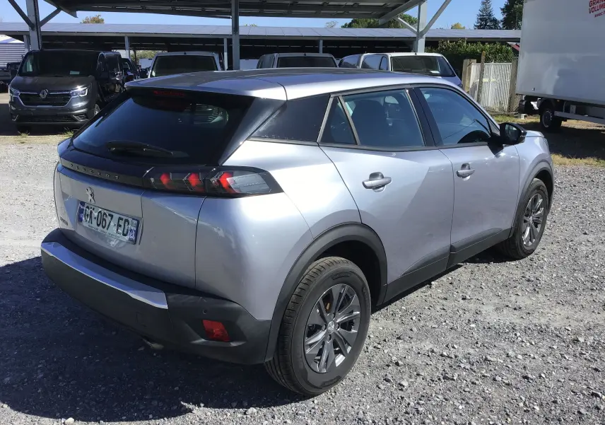 Peugeot 2008 gris Artense vue 3/4 arrière droit sur parking, avec toit noir et feux arrière distinctifs.