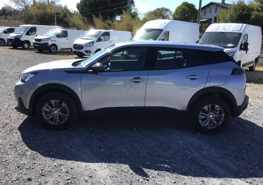 Peugeot 2008 gris Artense vue de profil côté gauche, avec toit noir et jantes alliage, stationnée sur un terrain gravillonné.