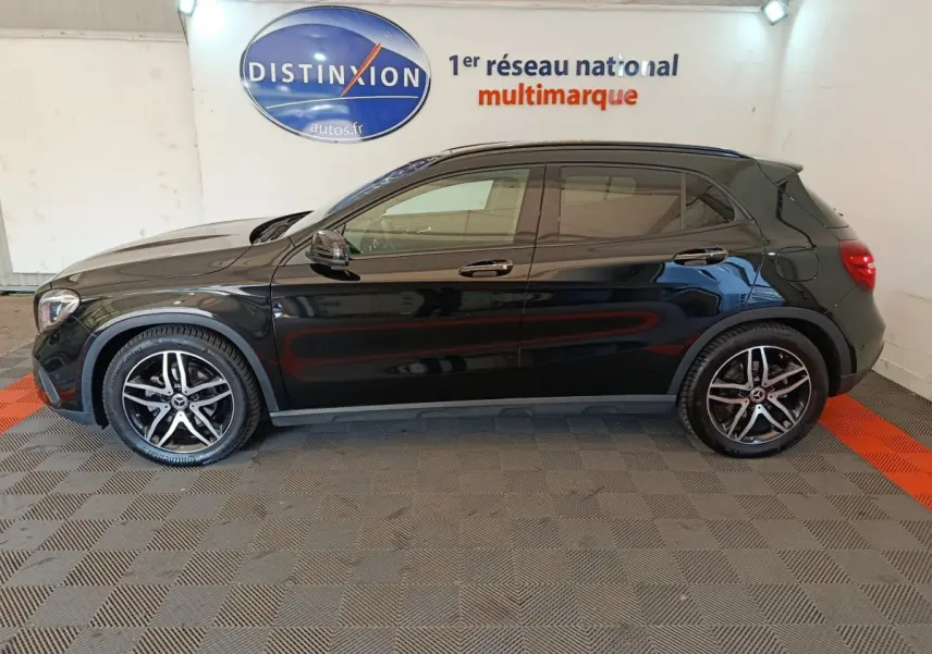 Vue de profil côté gauche d'un Mercedes GLA 220 d noir brillant avec jantes alliage et vitres teintées en intérieur showroom.