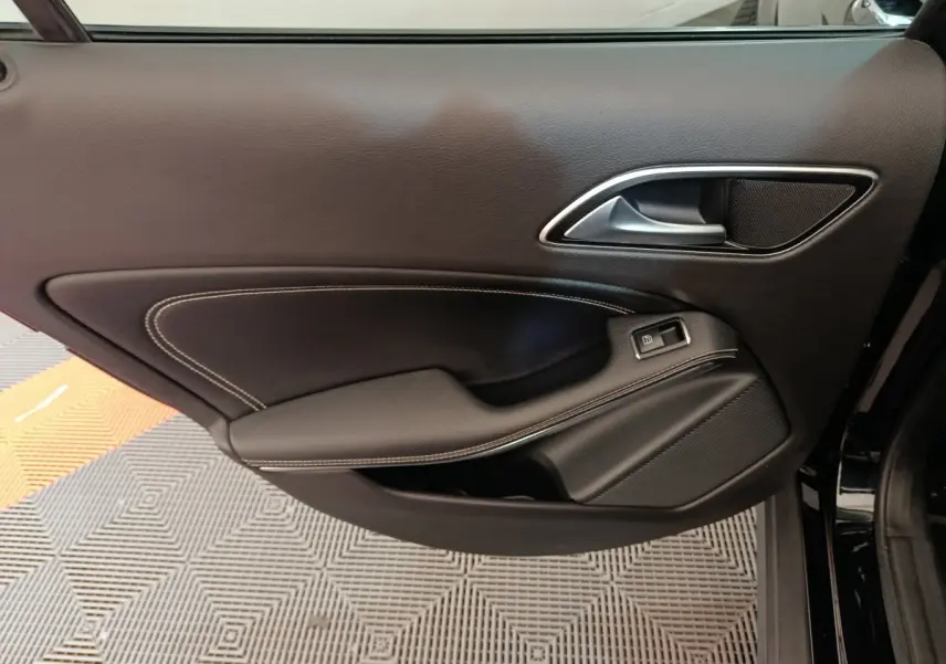 Gros plan sur la porte côté gauche noire du Mercedes GLA 220 d Business Exec avec surpiqûres blanches et poignée argentée.