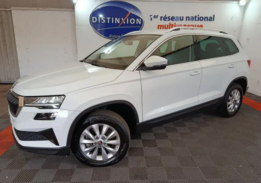 Vue 3/4 avant droite d'un Skoda Karoq blanc 2024 avec jantes alliage et barres de toit noires en showroom
