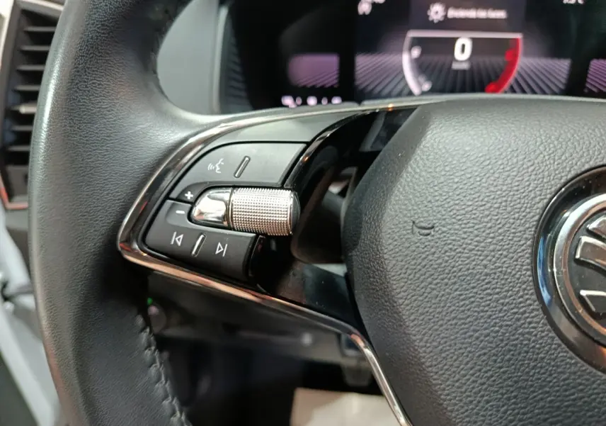 Gros plan sur la partie gauche du volant cuir noir du Skoda Karoq 2024 avec commandes audio et affichage numérique en arrière-plan.