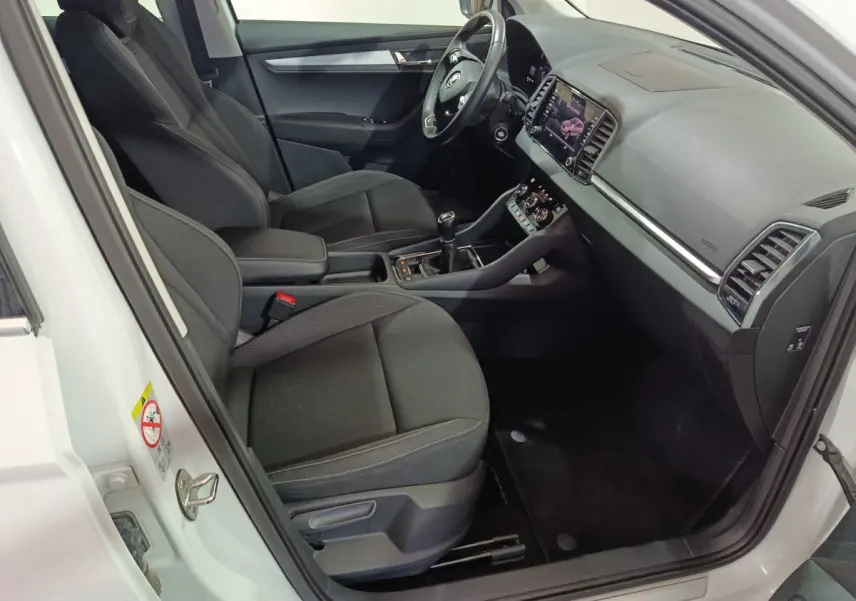 Intérieur avant droit d'un Skoda Karoq blanc 2024 avec sièges noirs, tableau de bord moderne et écran tactile central.