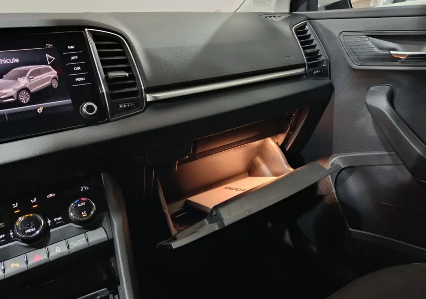 Intérieur noir du Skoda Karoq 2024, vue côté passager avec boîte à gants ouverte et écran tactile central allumé.