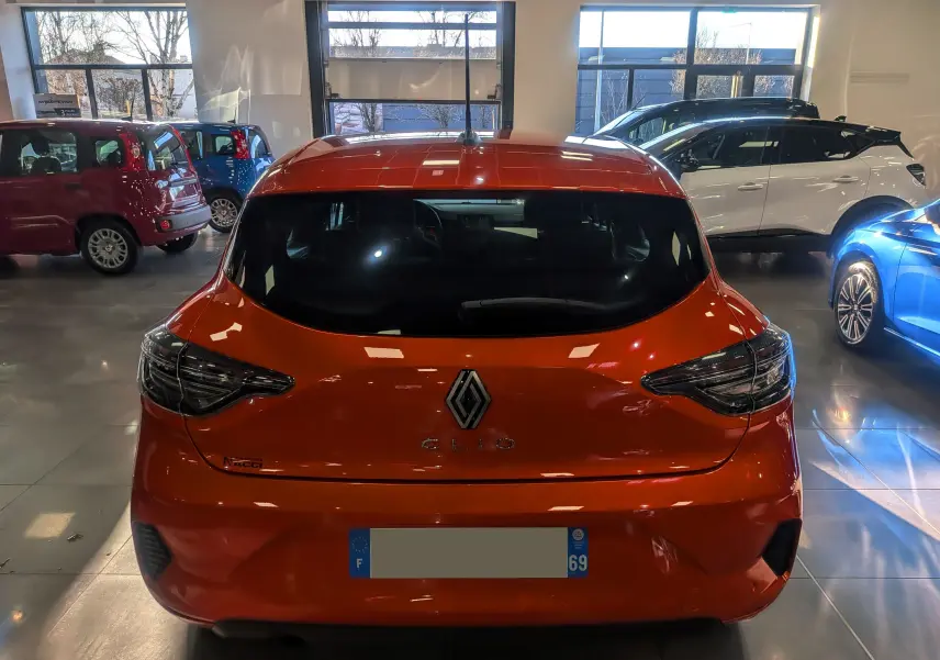Vue arrière d'une Renault Clio V Orange Valencia 2024 dans un showroom, avec feux arrière LED et caméra de recul visible.