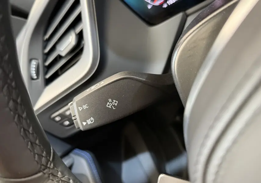 Gros plan sur la commande de clignotants noire dans l’habitacle d’une BMW Série 1 noire, avec tableau de bord partiellement visible.