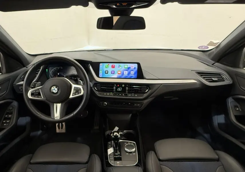 Vue intérieure avant de la BMW Série 1 120i Edition M Sport Pro 2023, tableau de bord noir avec écran tactile central.