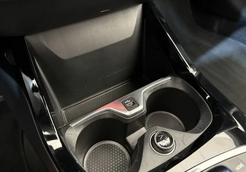 Gros plan sur la console centrale noire de la BMW Série 1 120i Edition M Sport Pro avec porte-gobelets et prise USB.