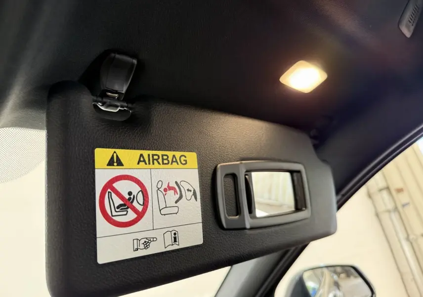 Détail de pare-soleil intérieur avec miroir et avertissement airbag, vue côté conducteur d’une BMW Série 1 noire.