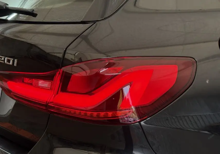 Gros plan sur le feu arrière droit rouge vif d'une BMW Série 1 120i noire, avec logo et partie de la carrosserie visible.