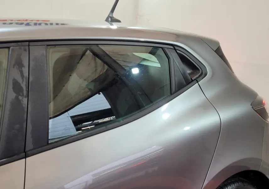 Vue latérale côté droit d'une Renault Clio gris foncé 2025, mettant en valeur la ligne fluide et la vitre arrière teintée.