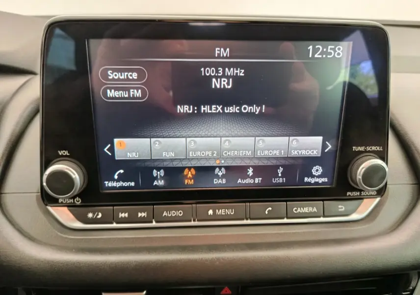 Écran tactile central du tableau de bord du Nissan Qashqai e-Power 2024 affichant la radio FM NRJ à 12h58.