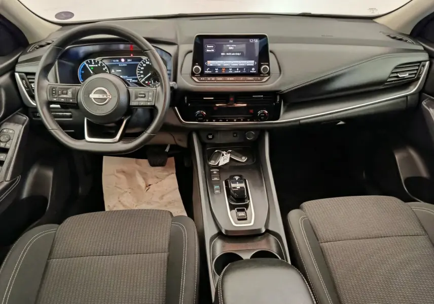 Vue intérieure avant du Nissan Qashqai e-Power 190 Business Edition 2024, tableau de bord noir avec écran tactile central et volant multifonctions.