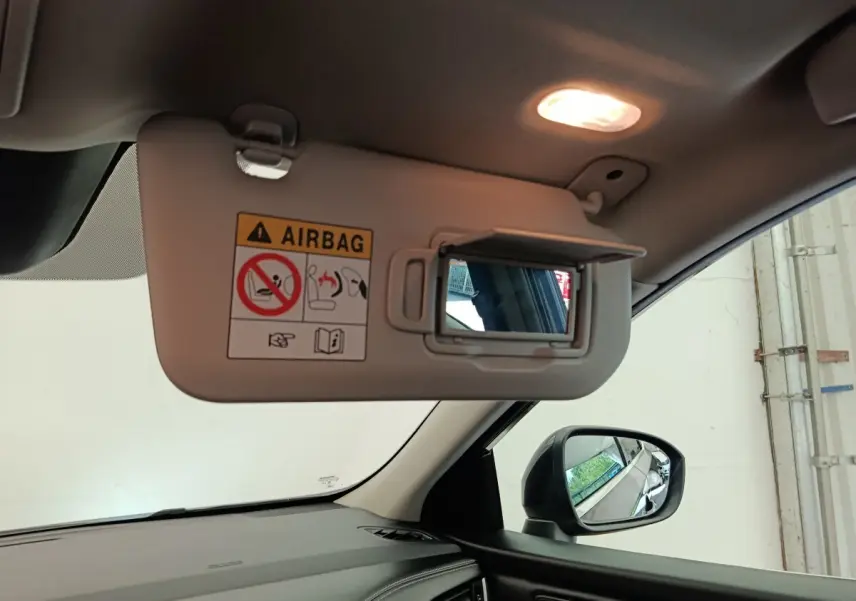 Détail intérieur du pare-soleil côté conducteur avec miroir et avertissement airbag, rétroviseur extérieur noir visible.