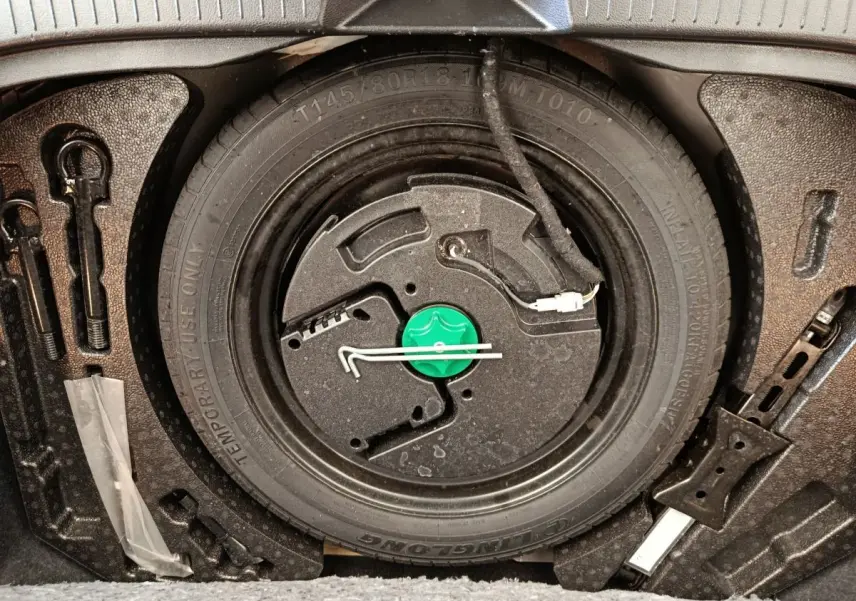 Gros plan sur la roue de secours galette noire et ses outils dans le coffre du Nissan Qashqai e-Power 2024.