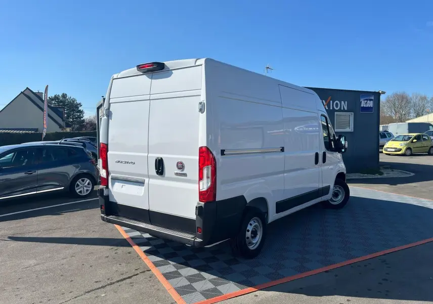 Vue 3/4 arrière droite d'un fourgon blanc FIAT Ducato 2023 avec portes arrière fermées sur parking extérieur.