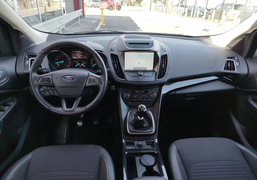 Vue intérieure du tableau de bord et volant noir du Ford Kuga 2019 avec boîte manuelle et écran tactile central.