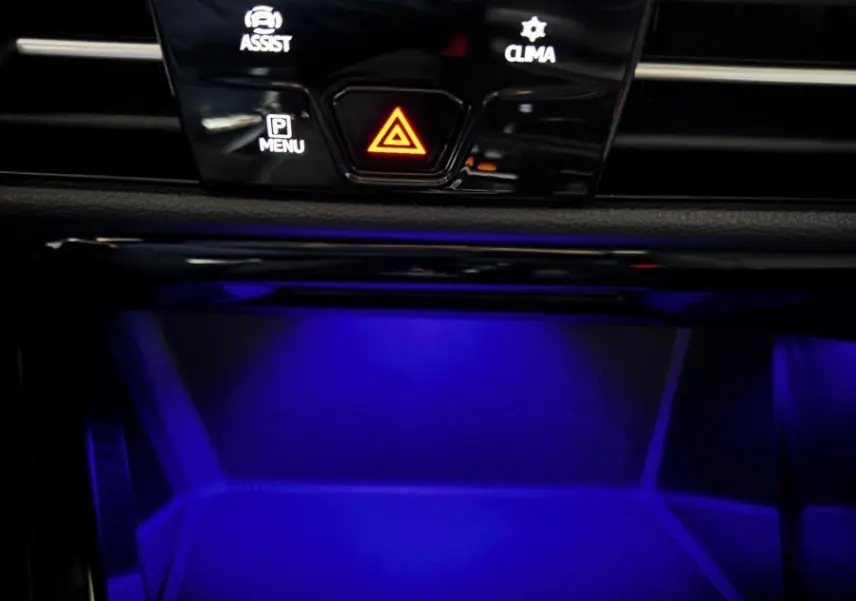 Détail du tableau de bord noir de la Volkswagen Golf 2024 avec éclairage d'ambiance bleu et boutons de contrôle au centre.