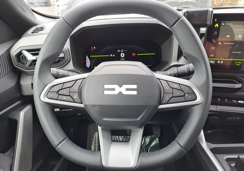 Vue rapprochée du volant noir du Dacia Bigster Hybrid 155 avec commandes intégrées et tableau de bord numérique.