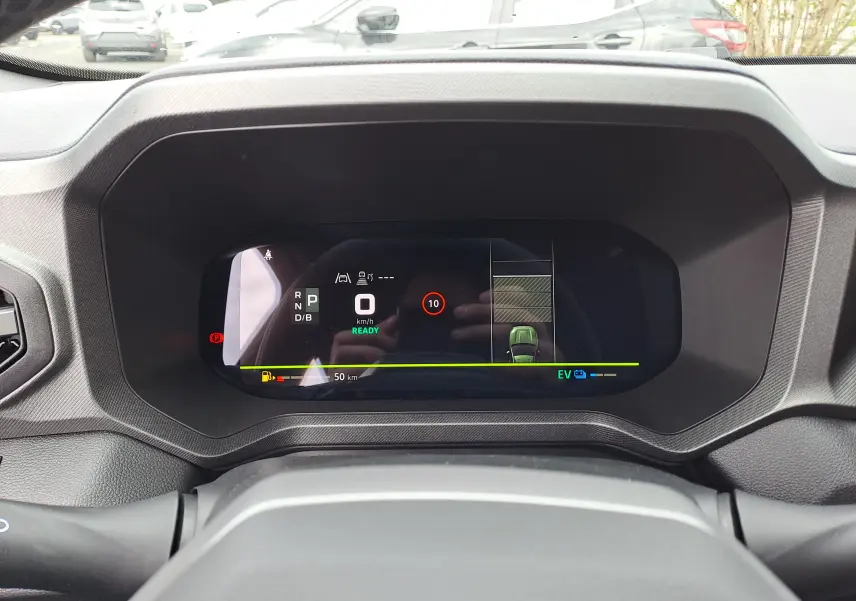 Vue intérieure du tableau de bord numérique du Dacia Bigster Hybrid 155, affichage de la vitesse et assistance au stationnement.