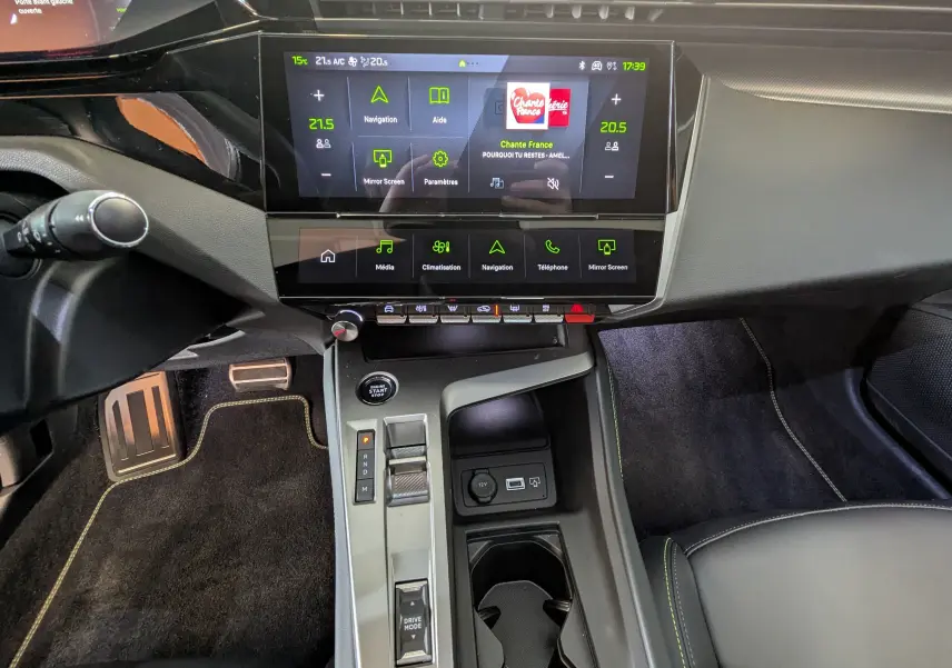 Vue intérieure centrée sur la console centrale et l’écran tactile du Peugeot 408 Hybrid blanc Okenite, avec commandes et pédales visibles.